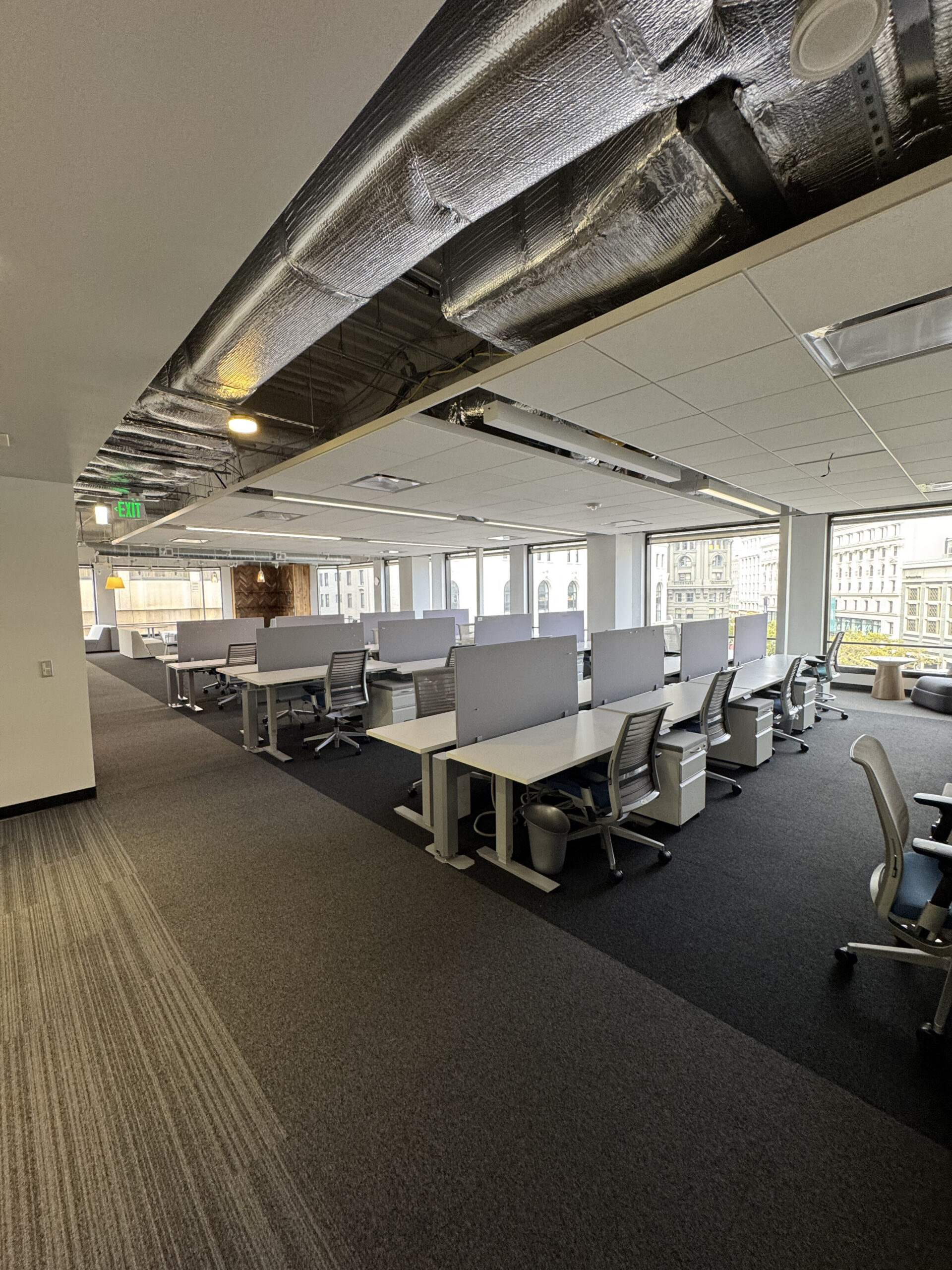 Open-plan office interior with desks, chairs, and large downtown windows